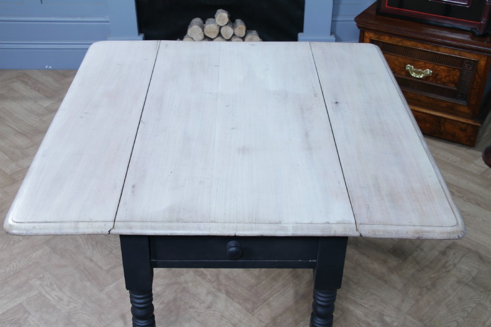 A restored Victorian Pembroke table featuring a bleached mahogany drop-leaf top and a black painted frame with turned legs on brass castors. View X