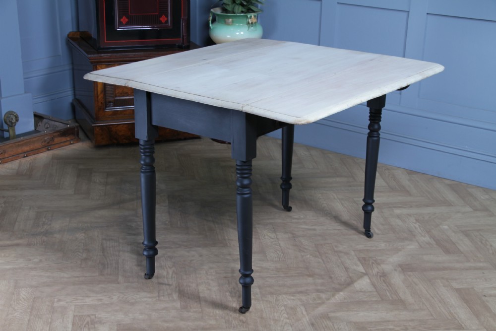 A restored Victorian Pembroke table featuring a bleached mahogany drop-leaf top and a black painted frame with turned legs on brass castors. View XXI