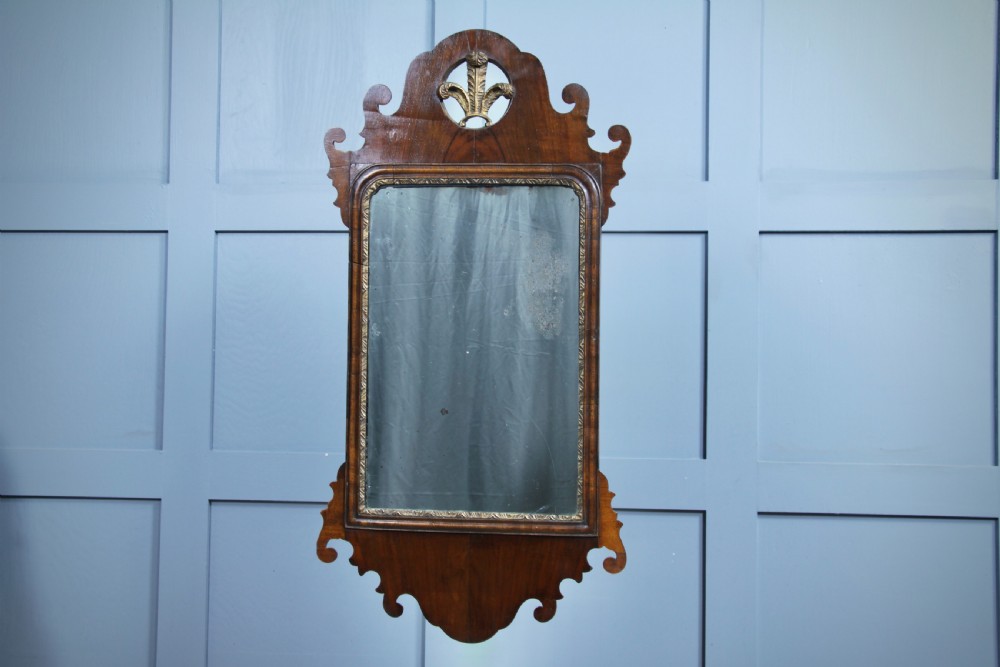A George III walnut wall mirror featuring silhouette scrollwork, a pierced crest with a gilded plume motif, and a glass plate with visible oxidisation.