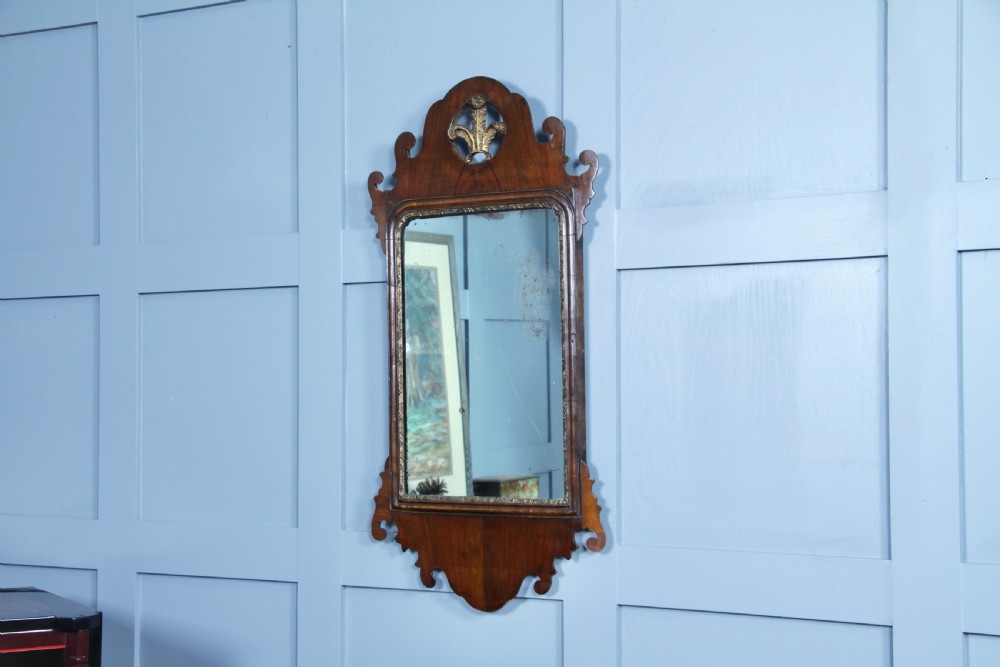 A George III walnut wall mirror featuring silhouette scrollwork, a pierced crest with a gilded plume motif, and a glass plate with visible oxidisation. View VI