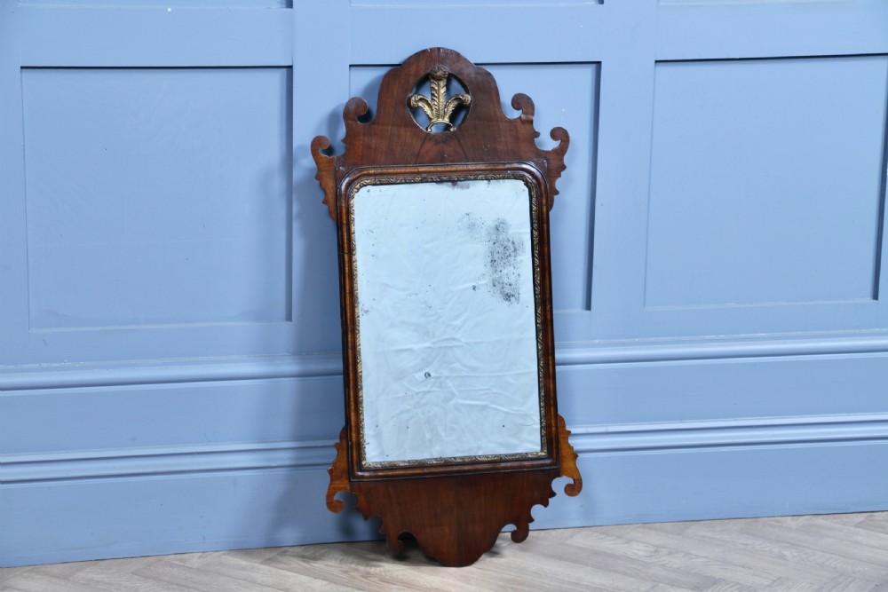 A George III walnut wall mirror featuring silhouette scrollwork, a pierced crest with a gilded plume motif, and a glass plate with visible oxidisation. View IX