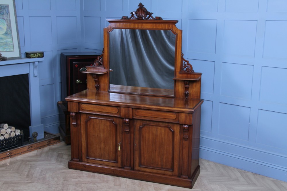 A Victorian mahogany mirror-back sideboard featuring two panelled cabinet doors, upper drawers, tiered side shelves, and a decorative carved cresting.