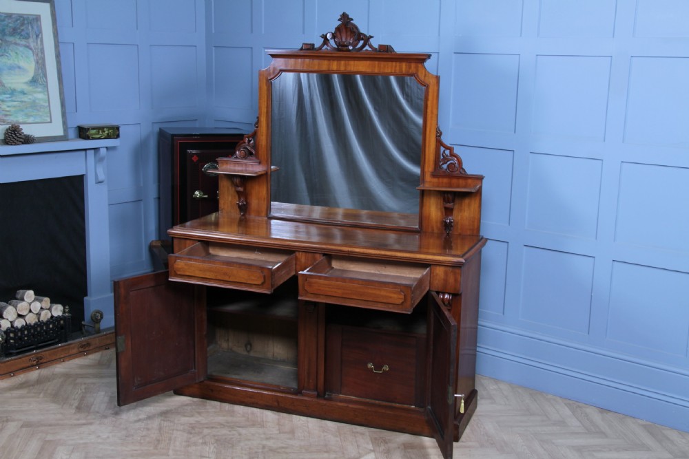 A Victorian mahogany mirror-back sideboard featuring two panelled cabinet doors, upper drawers, tiered side shelves, and a decorative carved cresting. View II