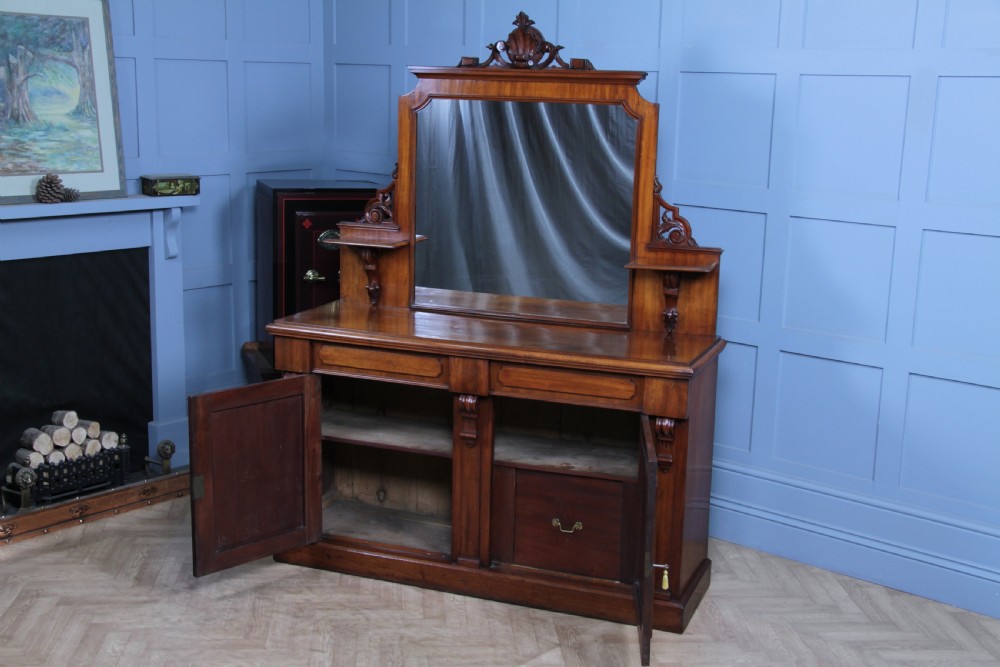 A Victorian mahogany mirror-back sideboard featuring two panelled cabinet doors, upper drawers, tiered side shelves, and a decorative carved cresting. View III