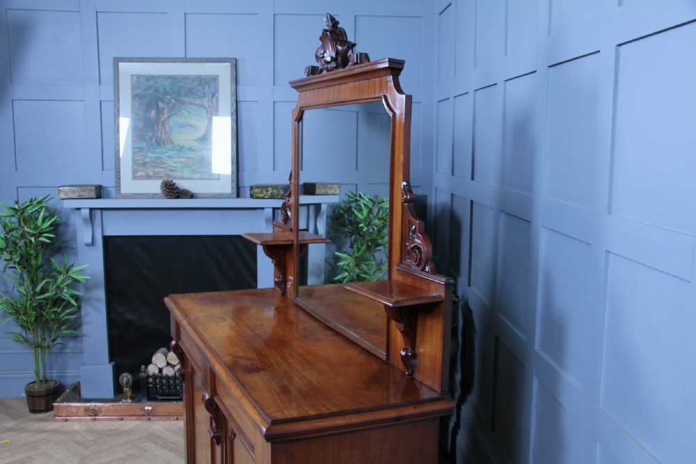 A Victorian mahogany mirror-back sideboard featuring two panelled cabinet doors, upper drawers, tiered side shelves, and a decorative carved cresting. View VI