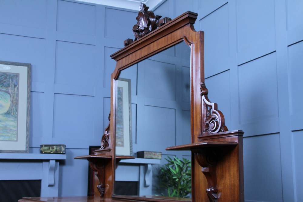 A Victorian mahogany mirror-back sideboard featuring two panelled cabinet doors, upper drawers, tiered side shelves, and a decorative carved cresting. View VII