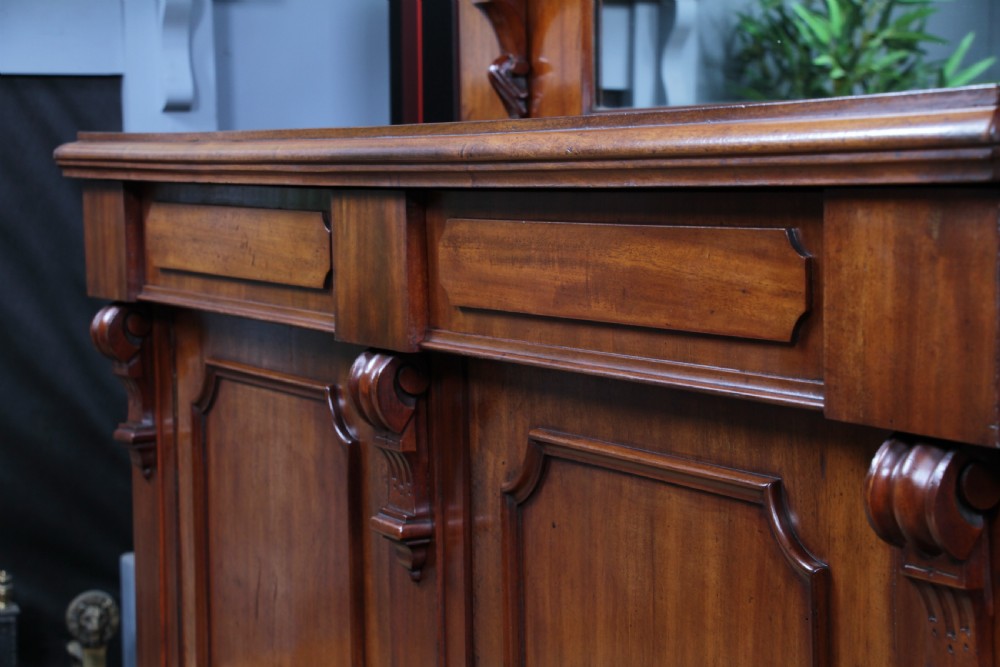 A Victorian mahogany mirror-back sideboard featuring two panelled cabinet doors, upper drawers, tiered side shelves, and a decorative carved cresting. View XII