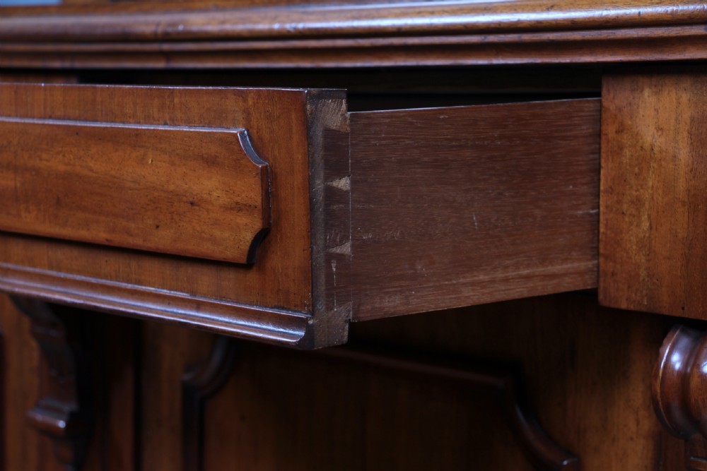 A Victorian mahogany mirror-back sideboard featuring two panelled cabinet doors, upper drawers, tiered side shelves, and a decorative carved cresting. View XIII