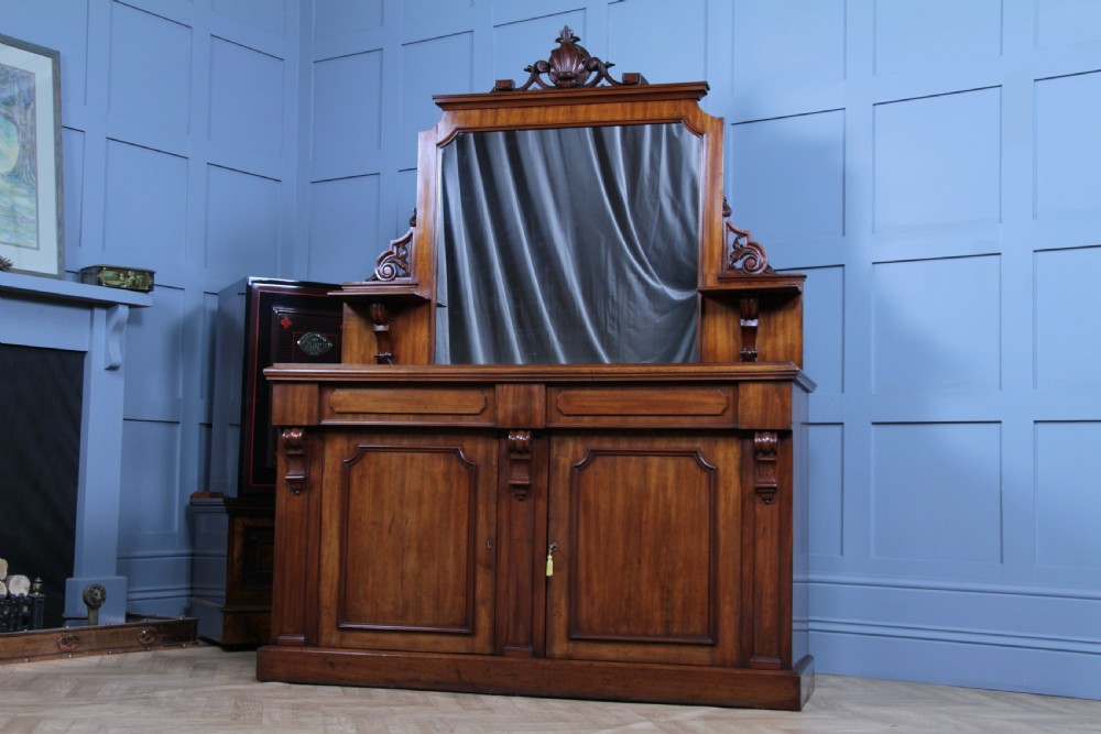 A Victorian mahogany mirror-back sideboard featuring two panelled cabinet doors, upper drawers, tiered side shelves, and a decorative carved cresting. View XIX