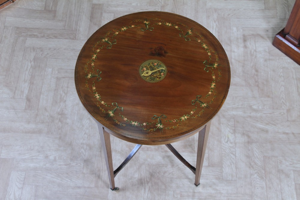 An Edwardian mahogany circular occasional table featuring a painted floral garland rim, central medallion, slender tapered legs, and an X-shaped cross-stretcher with a finial. View II