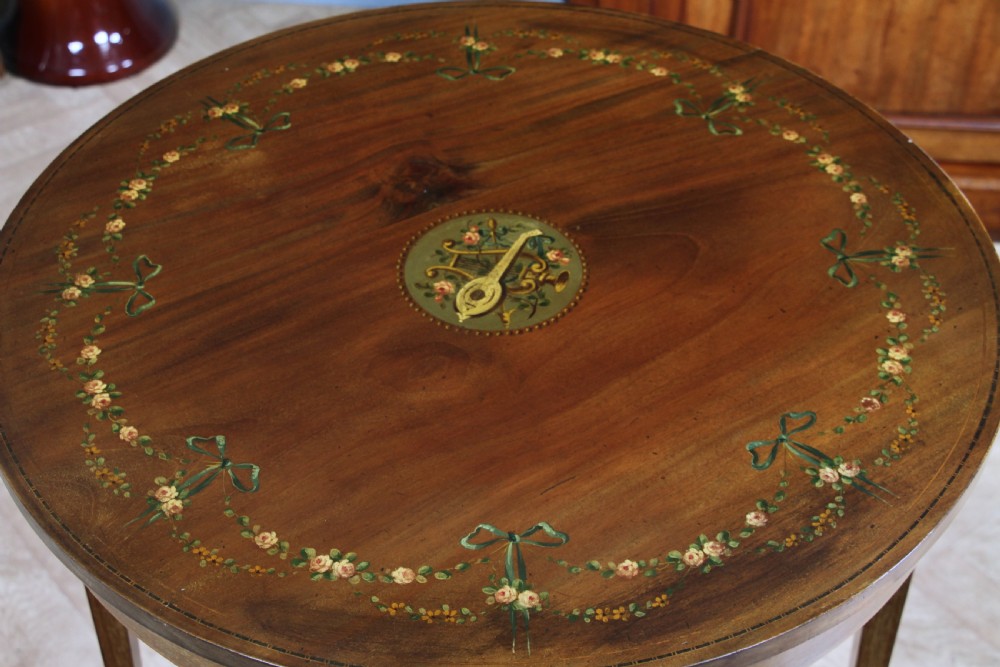 An Edwardian mahogany circular occasional table featuring a painted floral garland rim, central medallion, slender tapered legs, and an X-shaped cross-stretcher with a finial. View III