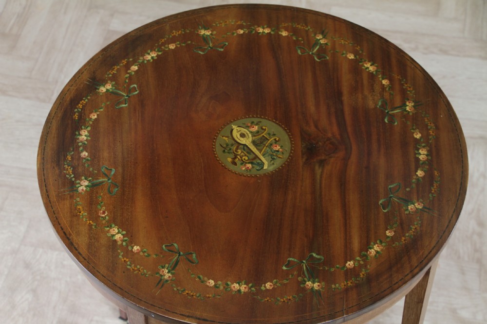 An Edwardian mahogany circular occasional table featuring a painted floral garland rim, central medallion, slender tapered legs, and an X-shaped cross-stretcher with a finial. View VII