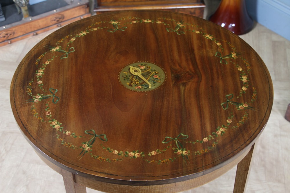 An Edwardian mahogany circular occasional table featuring a painted floral garland rim, central medallion, slender tapered legs, and an X-shaped cross-stretcher with a finial. View VIII
