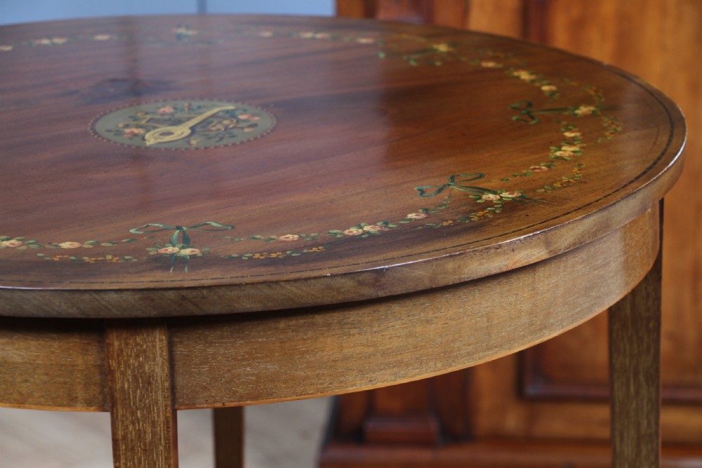 An Edwardian mahogany circular occasional table featuring a painted floral garland rim, central medallion, slender tapered legs, and an X-shaped cross-stretcher with a finial. View IX