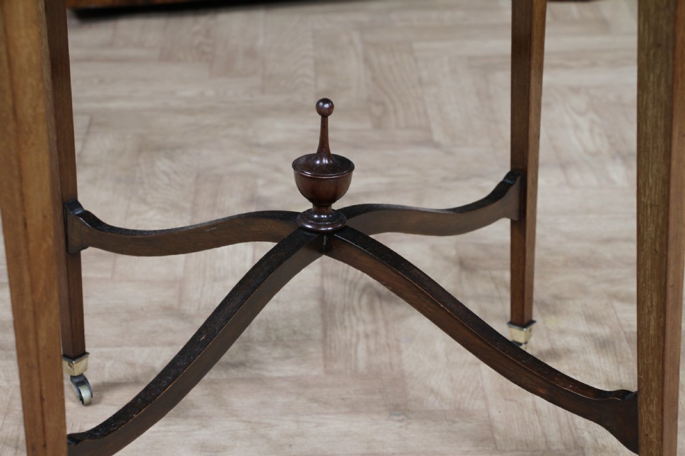 An Edwardian mahogany circular occasional table featuring a painted floral garland rim, central medallion, slender tapered legs, and an X-shaped cross-stretcher with a finial. View X