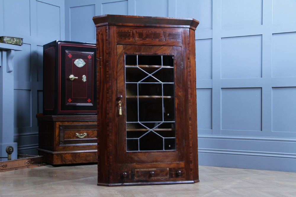 A Georgian mahogany wall-hanging corner cabinet featuring a single door with geometric glazed panels and a small base drawer.