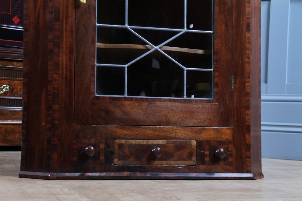 A Georgian mahogany wall-hanging corner cabinet featuring a single door with geometric glazed panels and a small base drawer. View II