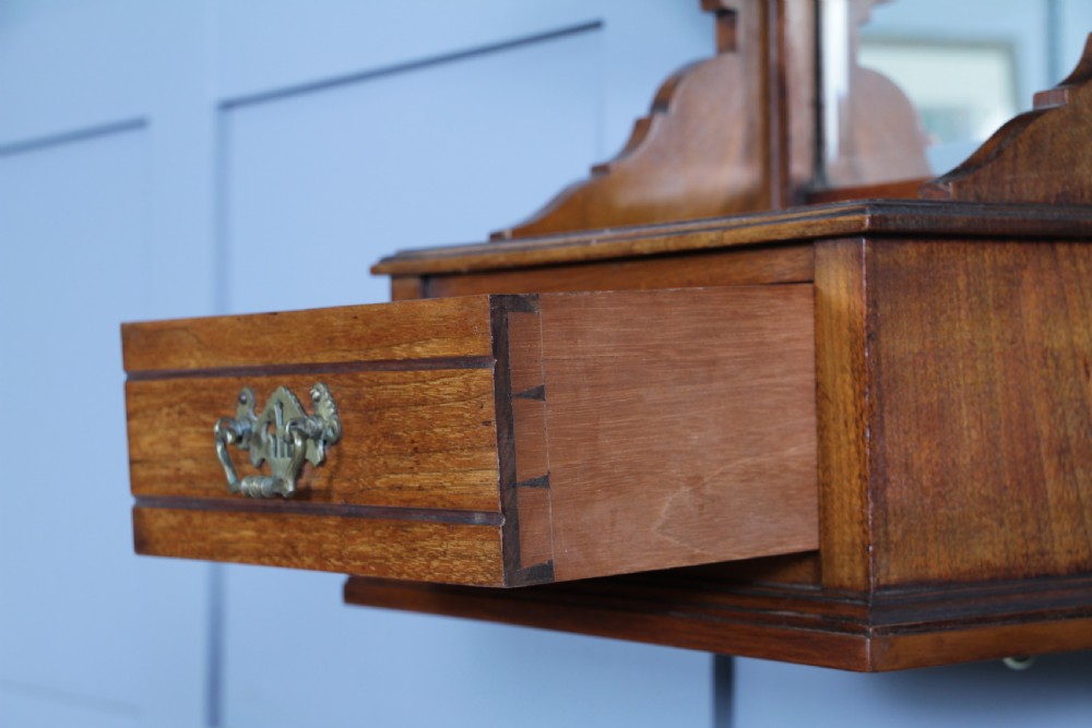 An Edwardian wall-mounted wooden cabinet featuring top finials, a carved floral panel, a central mirror, a lower drawer box with a brass handle, and bottom key hooks. View III