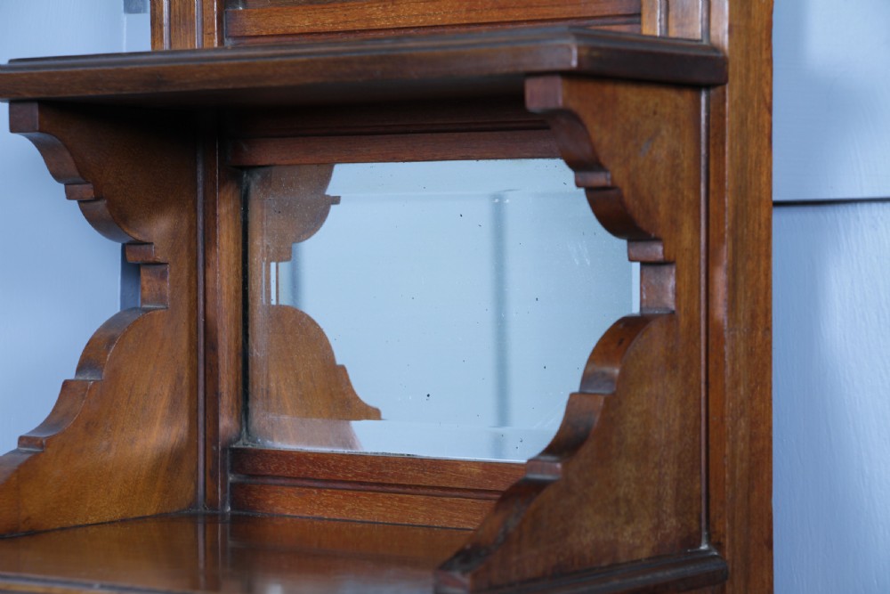 An Edwardian wall-mounted wooden cabinet featuring top finials, a carved floral panel, a central mirror, a lower drawer box with a brass handle, and bottom key hooks. View VI