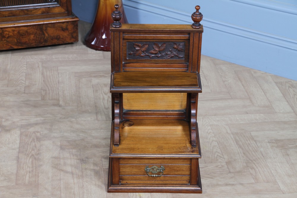 An Edwardian wall-mounted wooden cabinet featuring top finials, a carved floral panel, a central mirror, a lower drawer box with a brass handle, and bottom key hooks. View X