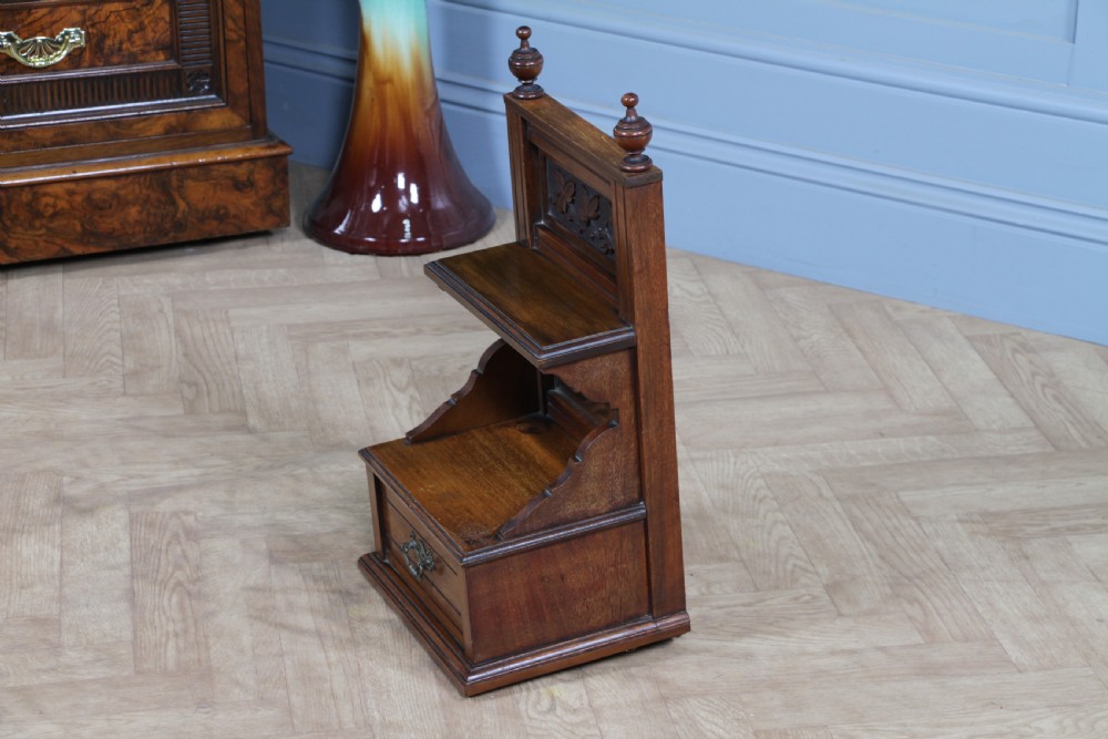An Edwardian wall-mounted wooden cabinet featuring top finials, a carved floral panel, a central mirror, a lower drawer box with a brass handle, and bottom key hooks. View XI