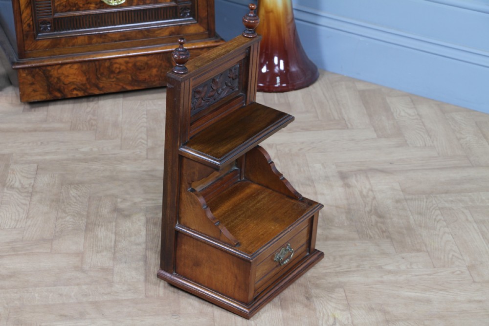 An Edwardian wall-mounted wooden cabinet featuring top finials, a carved floral panel, a central mirror, a lower drawer box with a brass handle, and bottom key hooks. View XII