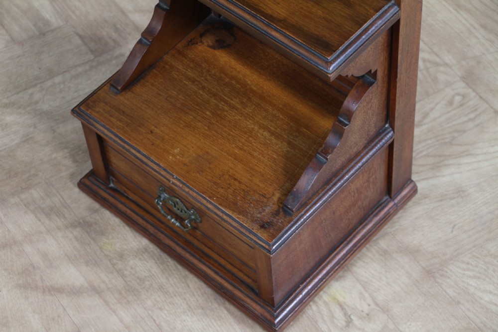 An Edwardian wall-mounted wooden cabinet featuring top finials, a carved floral panel, a central mirror, a lower drawer box with a brass handle, and bottom key hooks. View XIV