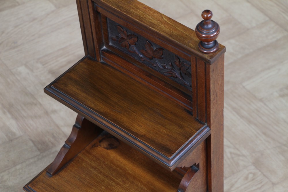 An Edwardian wall-mounted wooden cabinet featuring top finials, a carved floral panel, a central mirror, a lower drawer box with a brass handle, and bottom key hooks. View XV
