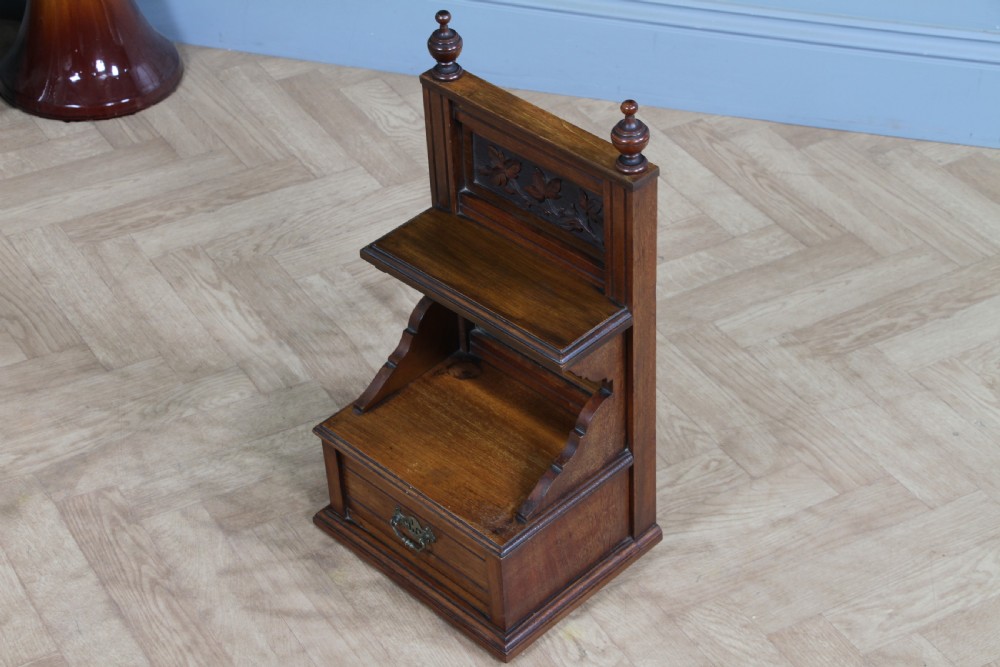 An Edwardian wall-mounted wooden cabinet featuring top finials, a carved floral panel, a central mirror, a lower drawer box with a brass handle, and bottom key hooks. View XVI