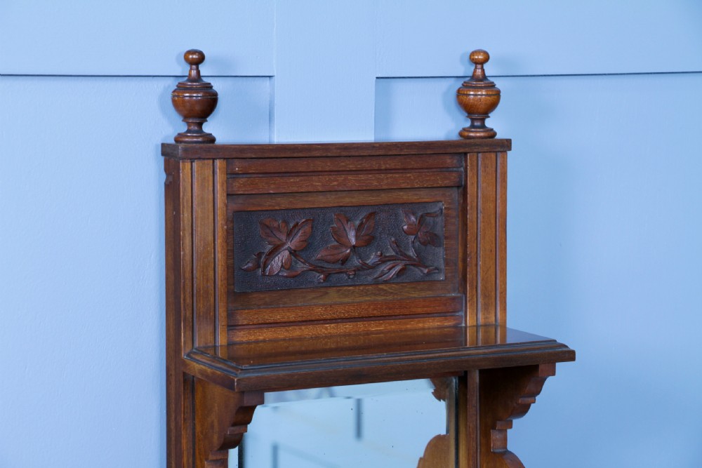 An Edwardian wall-mounted wooden cabinet featuring top finials, a carved floral panel, a central mirror, a lower drawer box with a brass handle, and bottom key hooks. View XVII
