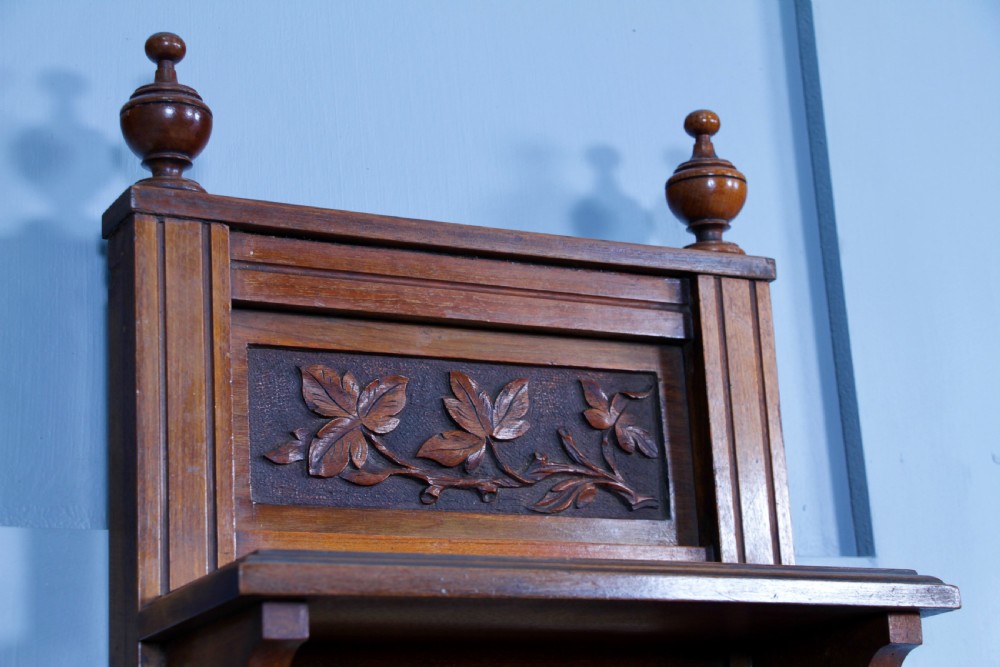 An Edwardian wall-mounted wooden cabinet featuring top finials, a carved floral panel, a central mirror, a lower drawer box with a brass handle, and bottom key hooks. View XVIII