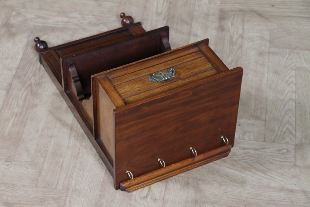 An Edwardian wall-mounted wooden cabinet featuring top finials, a carved floral panel, a central mirror, a lower drawer box with a brass handle, and bottom key hooks. View XXII