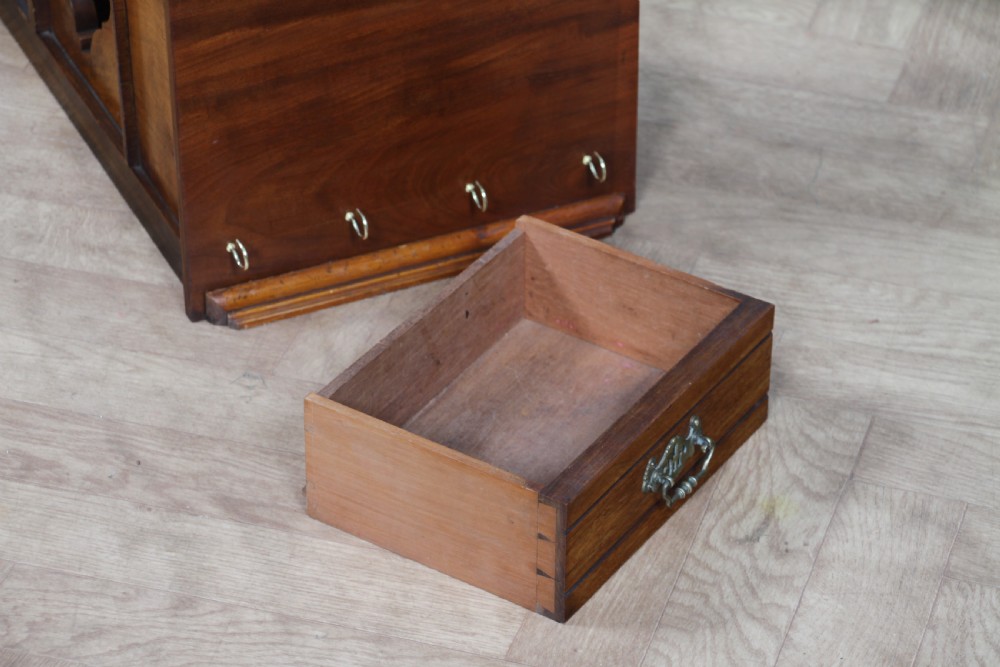 An Edwardian wall-mounted wooden cabinet featuring top finials, a carved floral panel, a central mirror, a lower drawer box with a brass handle, and bottom key hooks. View XXIII