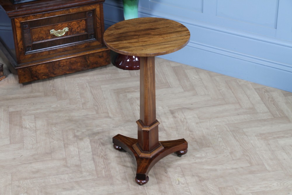 An antique William IV mahogany wine table featuring a circular top supported by a tapered faceted column and a triform base with bun feet.