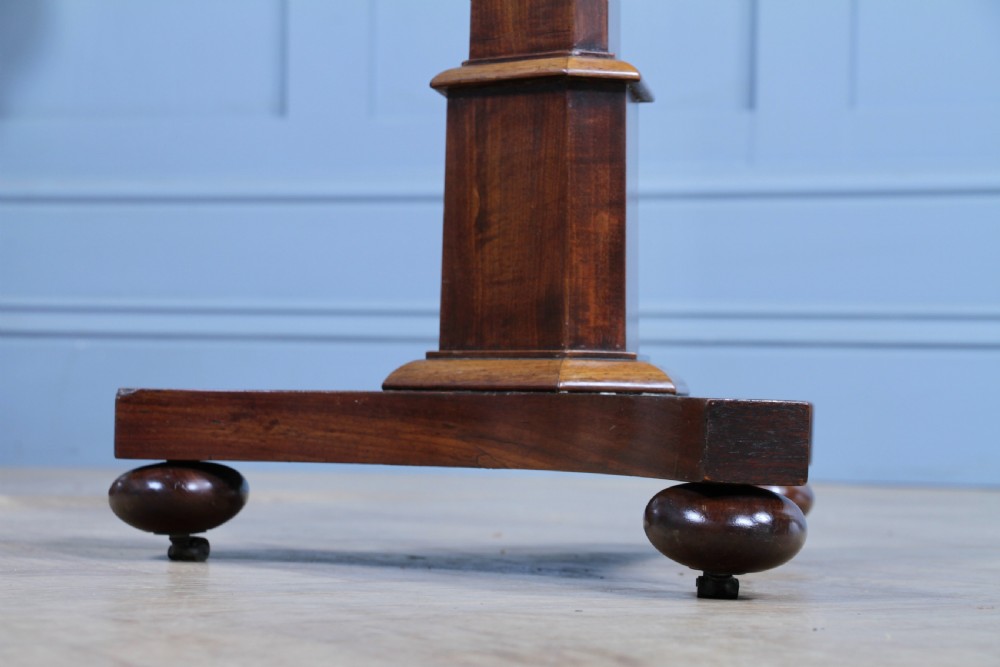 An antique William IV mahogany wine table featuring a circular top supported by a tapered faceted column and a triform base with bun feet. View XII