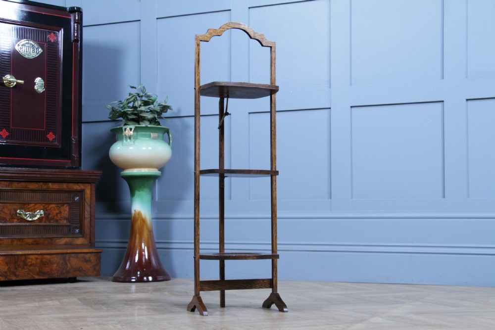 An Edwardian solid oak three-tier folding cake stand featuring square tiered shelves with recessed circular plate holders and an arched top handle. View III
