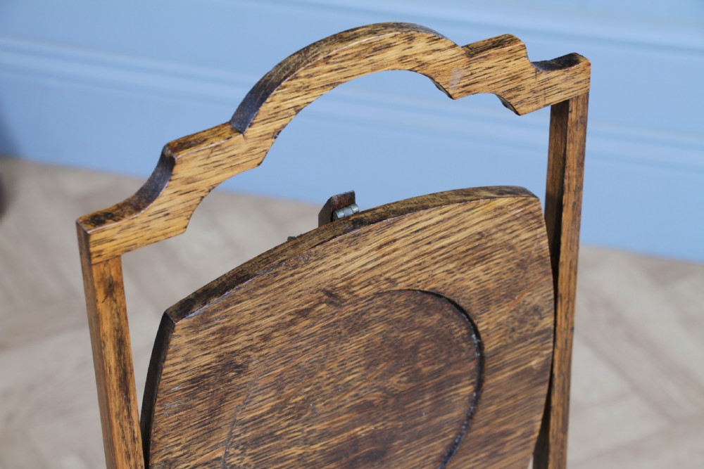 An Edwardian solid oak three-tier folding cake stand featuring square tiered shelves with recessed circular plate holders and an arched top handle. View V
