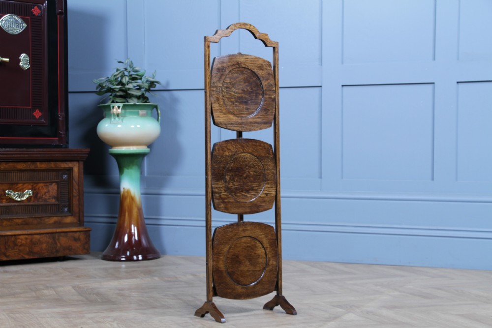 An Edwardian solid oak three-tier folding cake stand featuring square tiered shelves with recessed circular plate holders and an arched top handle. View VII