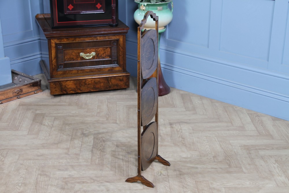 An Edwardian solid oak three-tier folding cake stand featuring square tiered shelves with recessed circular plate holders and an arched top handle. View VIII