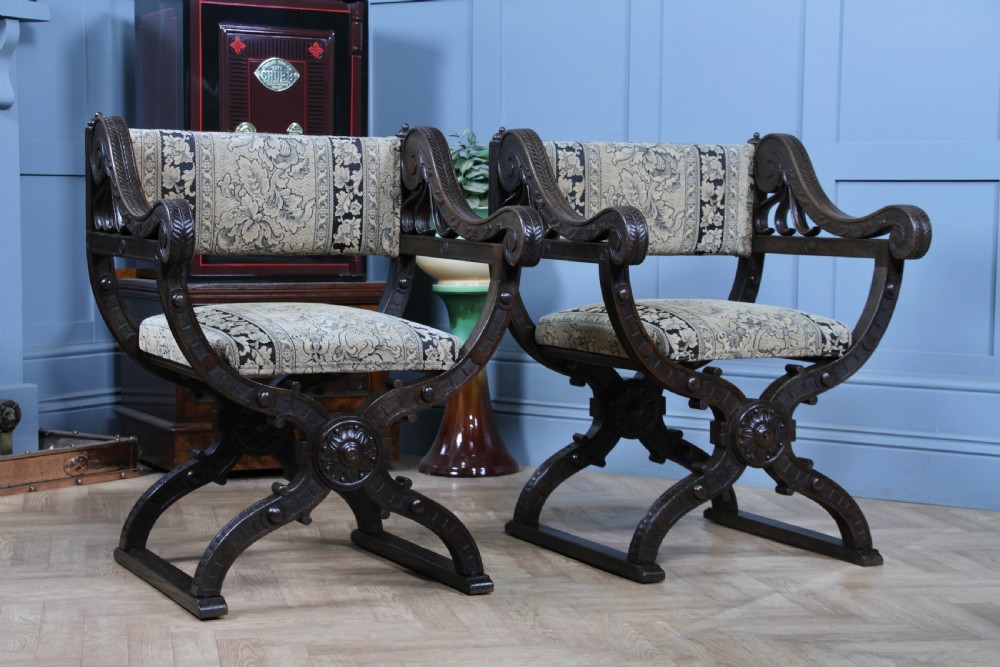 A pair of carved dark oak x-frame curule armchairs featuring patterned floral upholstery and central carved rosette bosses on the legs. View II
