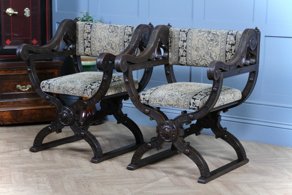A pair of carved dark oak x-frame curule armchairs featuring patterned floral upholstery and central carved rosette bosses on the legs. View III