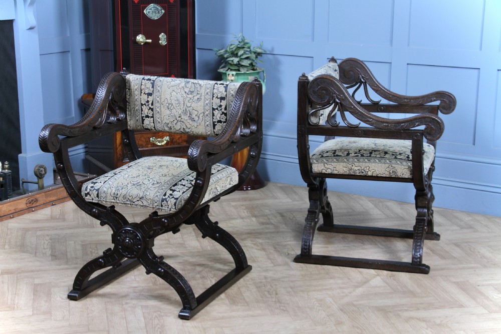 A pair of carved dark oak x-frame curule armchairs featuring patterned floral upholstery and central carved rosette bosses on the legs. View V