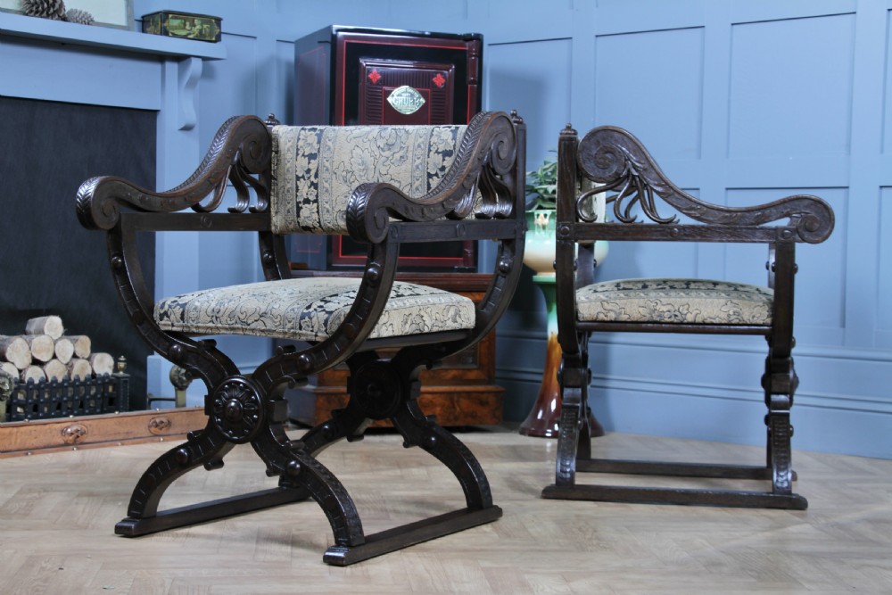 A pair of carved dark oak x-frame curule armchairs featuring patterned floral upholstery and central carved rosette bosses on the legs. View VI
