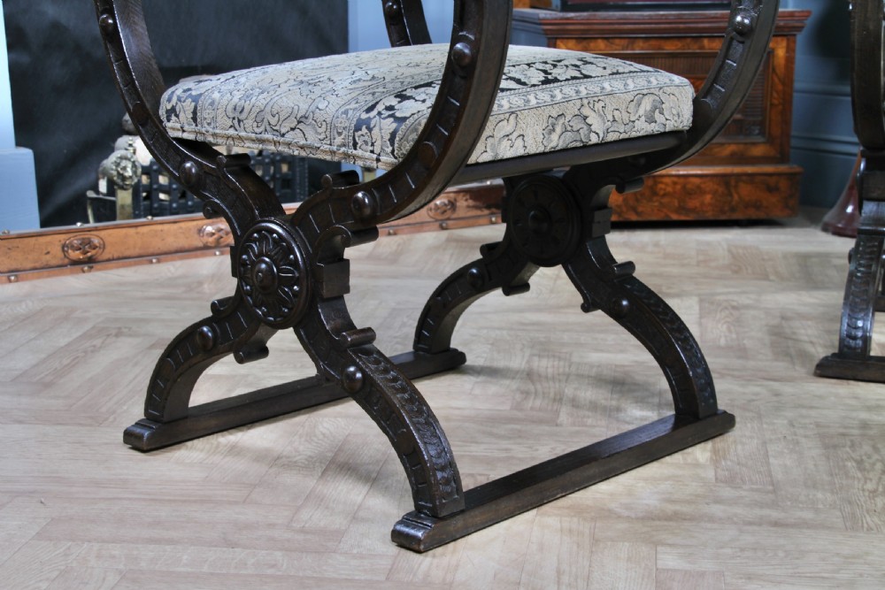 A pair of carved dark oak x-frame curule armchairs featuring patterned floral upholstery and central carved rosette bosses on the legs. View VII