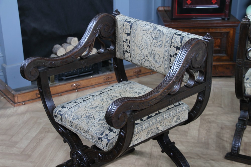 A pair of carved dark oak x-frame curule armchairs featuring patterned floral upholstery and central carved rosette bosses on the legs. View VIII