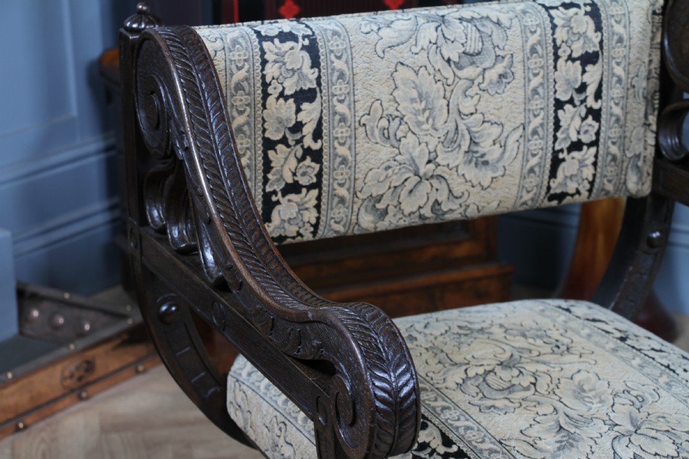 A pair of carved dark oak x-frame curule armchairs featuring patterned floral upholstery and central carved rosette bosses on the legs. View XI
