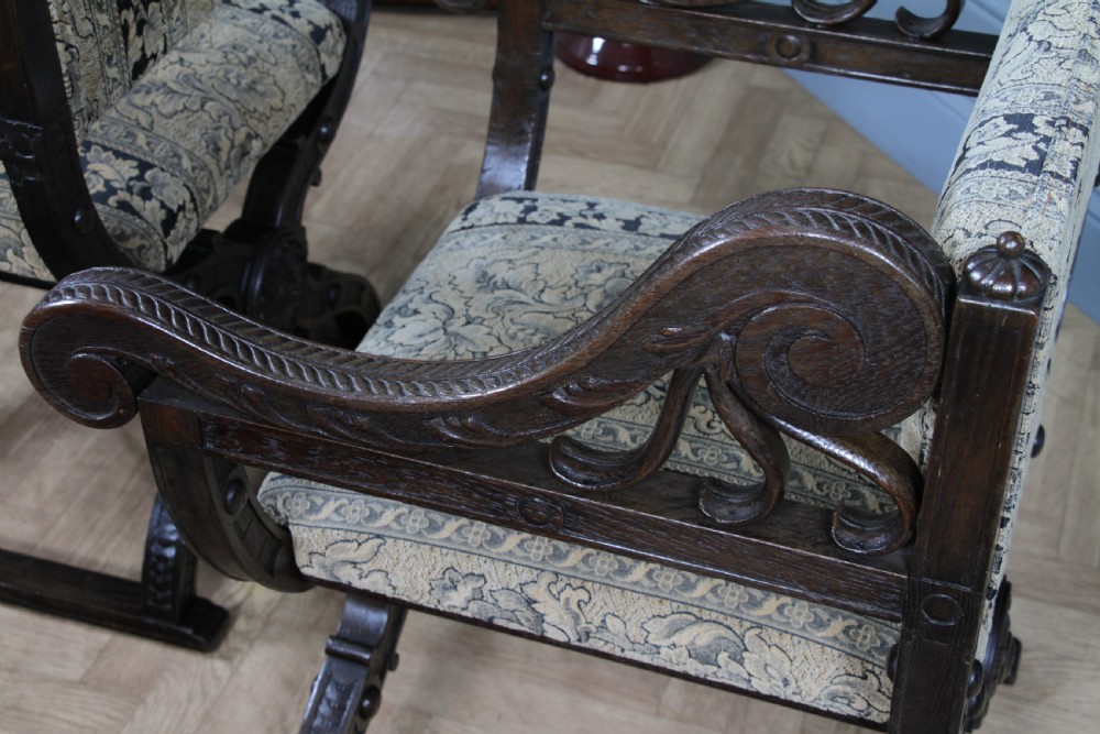A pair of carved dark oak x-frame curule armchairs featuring patterned floral upholstery and central carved rosette bosses on the legs. View XIII
