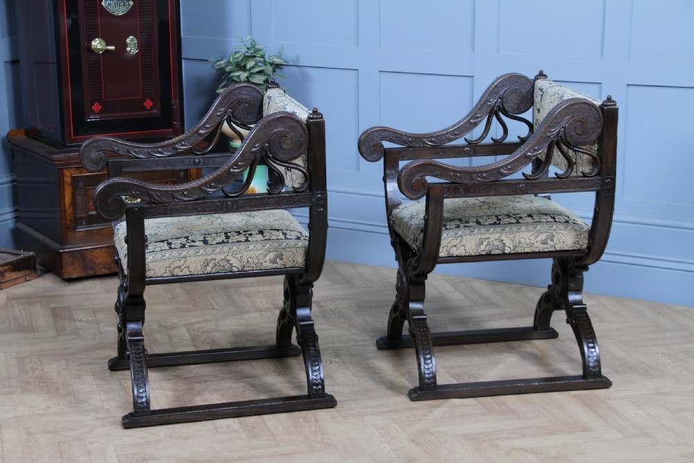 A pair of carved dark oak x-frame curule armchairs featuring patterned floral upholstery and central carved rosette bosses on the legs. View XVII