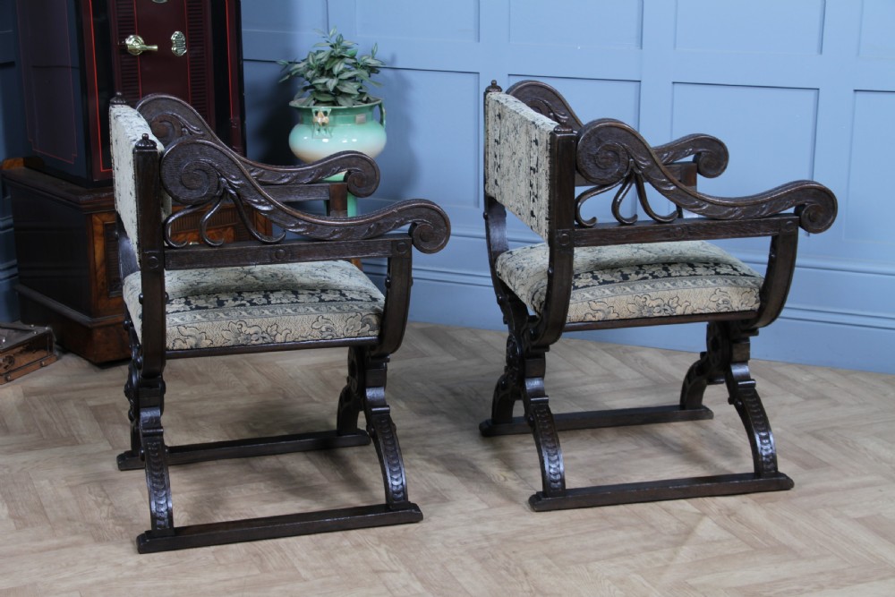A pair of carved dark oak x-frame curule armchairs featuring patterned floral upholstery and central carved rosette bosses on the legs. View XVIII