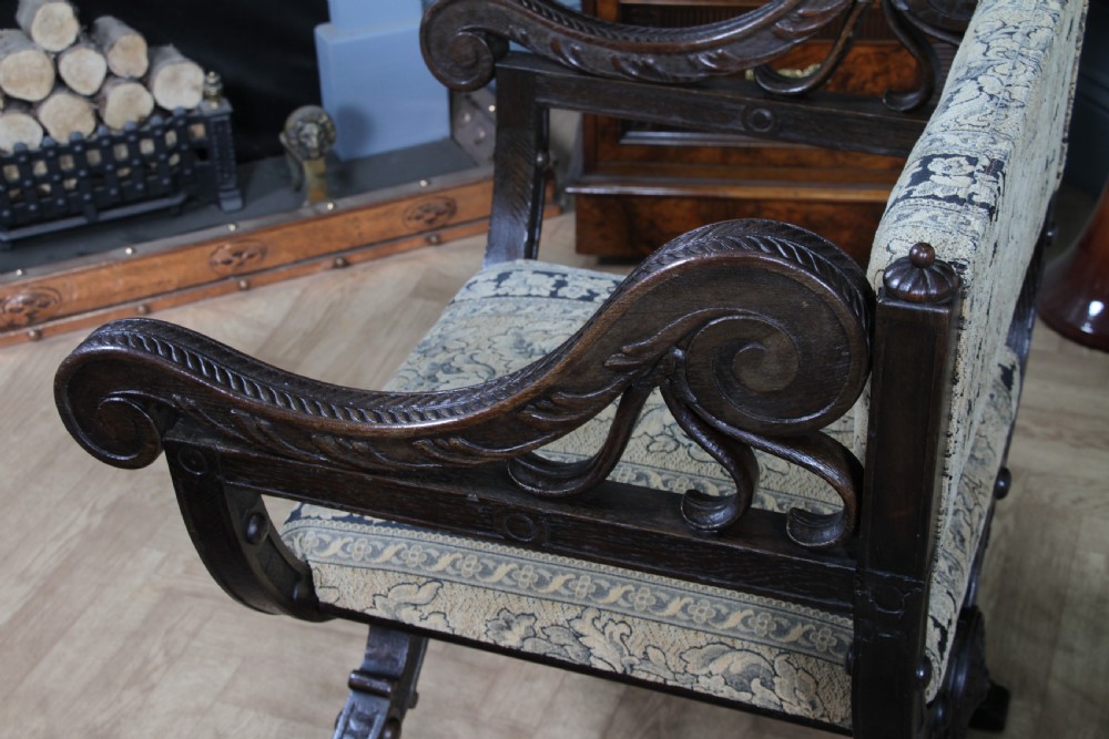 A pair of carved dark oak x-frame curule armchairs featuring patterned floral upholstery and central carved rosette bosses on the legs. View XX